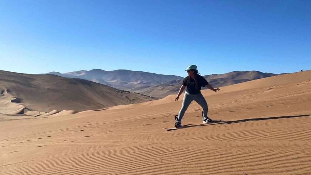 Haciendo sandboard en atacama, donde un turista deslizandose por el mar de dunas, disfrutando la aventura